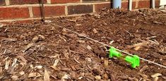 there is a green plastic toy in the mulch next to a brick wall and fence