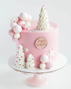 a pink christmas cake with white decorations and trees on the top, sitting on a plate