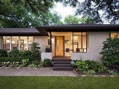 a small house that is in the middle of some grass and trees with bushes around it