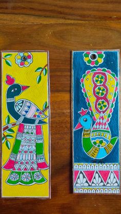 two colorful painted bookmarks sitting on top of a wooden table