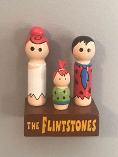 three wooden toy figures on top of a sign that says the flintstones and two other figurines