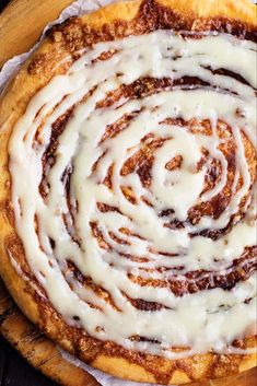 a cinnamon roll with icing sitting on top of a wooden cutting board