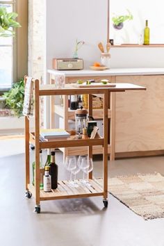 a kitchen cart with wine glasses and bottles on it in the middle of a room