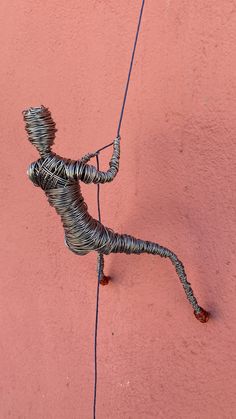 a wire sculpture on the side of a pink wall with a string attached to it