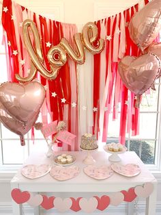 a table topped with lots of pink and gold heart shaped balloons next to a window