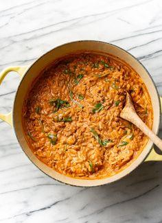 a pot filled with rice and vegetables on top of a marble countertop next to a wooden spoon