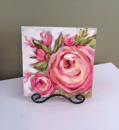 a painting of pink roses on a white table with a black metal holder for it