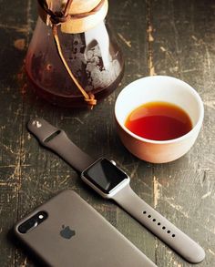 an apple watch and cup of tea sit on a table next to a cell phone