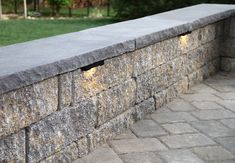 a stone wall with two lights on it and some grass in the backround