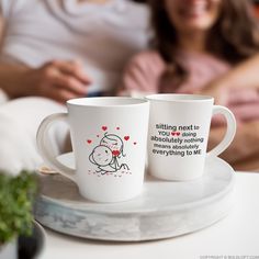 two coffee mugs sitting on top of a white plate next to a woman and child