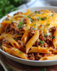 a white bowl filled with pasta covered in ground beef and cheese on top of a wooden cutting board