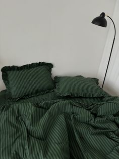 an unmade bed with green striped sheets and pillows on it, next to a black lamp