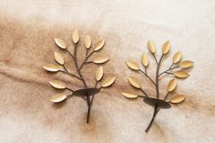 two metal wall hangings made to look like branches with leaves on them sitting on a fur surface