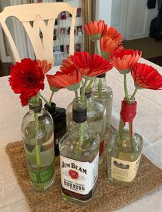 four bottles with flowers in them sitting on a placemat next to two empty liquor bottles