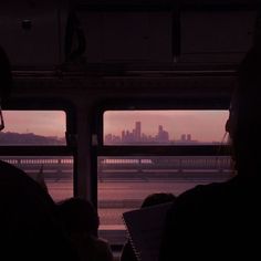 people are sitting on a bus looking out the window at the water and buildings in the distance