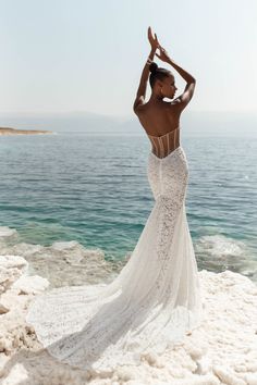 a woman in a white wedding dress standing on the beach with her arms above her head