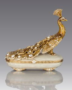 a golden peacock figurine sitting on top of a white base