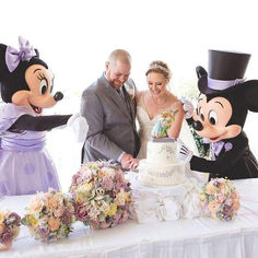 a newly married couple cutting their wedding cake with mickey and minnie mouse heads in the background