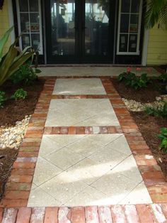 a walkway made out of bricks leads to a front door with glass doors and palm trees in the background