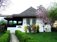 a white house surrounded by lush green grass and trees with pink flowers on the roof