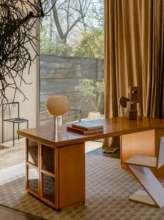 a wooden desk sitting in front of a window next to a book shelf and lamp