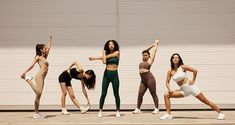 five women in sports wear are standing on the side walk and stretching their arms up