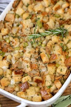 a casserole dish filled with stuffing and topped with fresh herbs on a wooden table