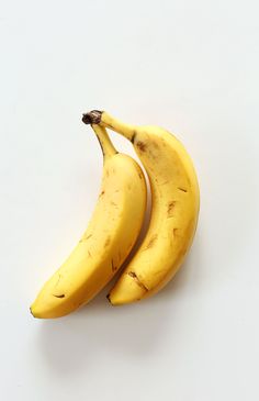 two ripe bananas sitting next to each other on a white surface