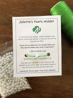 a package of pearls next to a spool of thread on a wooden table with a green needle