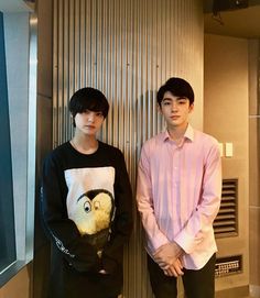 two young men standing next to each other in front of a wall with an owl on it