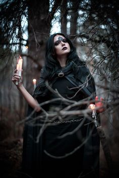 a woman holding a candle standing in the woods