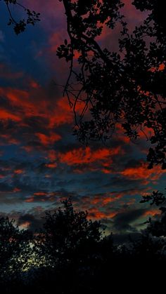 the sky is red and blue at night with some clouds in the foreground, trees to the right