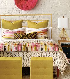 a bed with pillows, blankets and footstools in front of a white brick wall