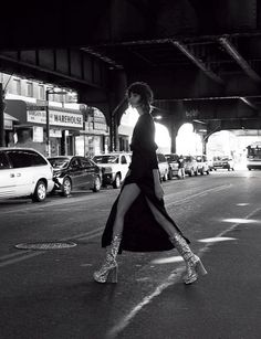 black and white photograph of woman walking in the middle of an urban street at night