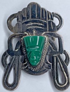 a brooch with a green face on it's side and two metal handles