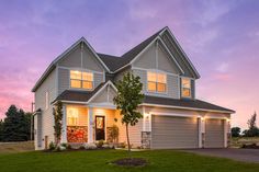 a large house with lights on in the front yard at dusk, lit up by outdoor lighting