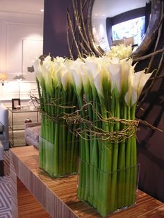 two vases filled with white flowers sitting on top of a wooden table next to a mirror