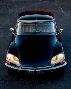 an old black car parked in a parking lot with its hood up and lights on