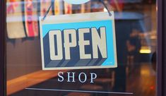 an open sign hanging from the window of a shop