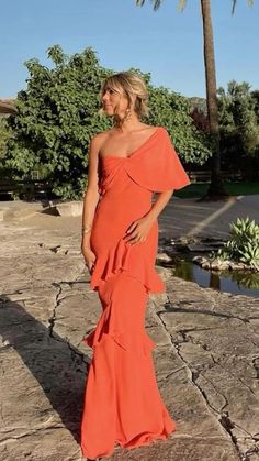 a woman in an orange dress is standing on the rocks near some water and palm trees