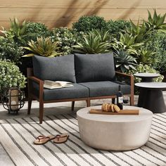 a couch and coffee table on a rug in front of some bushes with plants around it