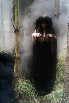 a woman standing in the woods with her hands on her chest and wearing a long black dress