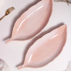 two pink leaves sitting on top of a white table next to a fork and spoon