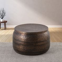 a large round metal ottoman sitting on top of a carpeted floor next to a table