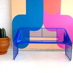 a blue bench sitting next to a potted plant in front of a colorful wall