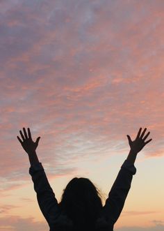 a woman with her arms up in the air at sunset or dawn, reaching out to catch a frisbee