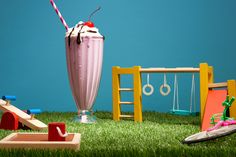 an ice cream sundae in a tall glass on top of green grass next to toys