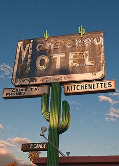 an old motel sign on top of a green cactus in front of a blue sky