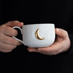 a person holding a coffee cup with a crescent decoration on the side and gold rim