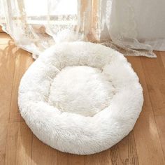 a white dog bed sitting on top of a wooden floor in front of a window